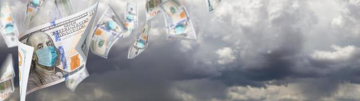 100-Dollar-Scheine mit medizinischer Gesichtsmaske, die vom Banner des stürmischen bewölkten Himmels fallen foto