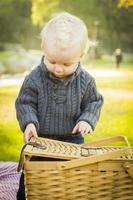 Blonder kleiner Junge öffnet Picknickkorb im Freien im Park foto