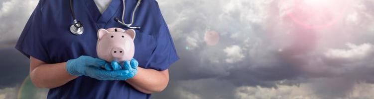 arzt oder krankenschwester tragen chirurgische handschuhe, die sparschwein über wolkenbanner halten foto