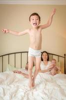 Chinesischer und kaukasischer Junge mit gemischten Rassen, der mit seiner Familie ins Bett springt foto
