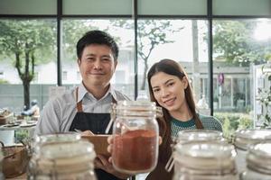 Porträt von zwei Ladenbesitzern mit natürlichen Bio-Produkten in wiederverwendbaren Gläsern, Lächeln und Blick in die Kamera im Nachfüllladen, Zero Waste, plastikfreie Lebensmittel und umweltfreundliches, nachhaltiges Geschäft. foto