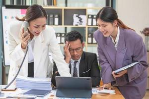 Ein Team von drei asiatischen Geschäftsleuten arbeitet in einem Büro, in dem Geschäftsleute in schwarzen Anzügen von ihren Vorgesetzten und Chefs viel bestellt werden, was zu Stress bei der Arbeit führt. Burnout-Konzept foto