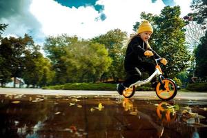 süßes kleines Mädchen fährt mit dem Fahrrad im Park durch die Pfützen foto