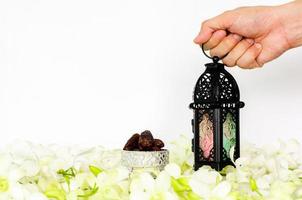 Hand, die Laterne auf weißem Hintergrund mit Dattelfrüchten auf Orchideenblüte für das muslimische Fest des heiligen Monats Ramadan Kareem hält. foto