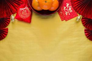 chinesisches neujahrskonzept mit roten umschlagpaketen oder ang bao-wort bedeuten glücksvorzeichen, orangen, barren und rotes taschenwort bedeuten reichtum auf goldleerem raumhintergrund mit roten fächern. foto