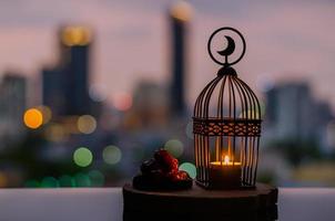 laterne mit mondsymbol oben und dattelfrüchten auf holztablett mit bunten stadt-bokeh-lichtern für das muslimische fest des heiligen monats ramadan kareem. foto