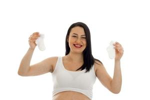 fröhliche junge schwangere brünette Frau mit zwei kleinen Socken in den Händen lächelnd isoliert auf weißem Hintergrund foto