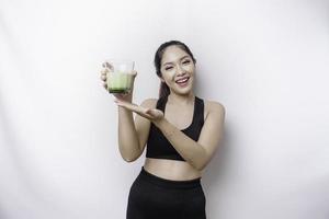 Fröhliche, sportliche asiatische Frau, die Sportkleidung mit einem Glas leckeren grünen Smoothie trägt, isoliert auf weißem Hintergrund. foto