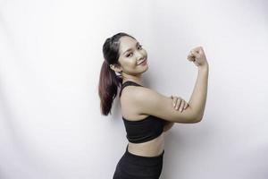 Aufgeregte asiatische sportliche Frau, die eine Sportkleidung trägt, die eine starke Geste zeigt, indem sie stolz ihre Arme und Muskeln hebt und lächelt foto
