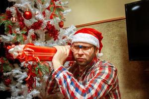 seriöser nerd in stana hut mit langem weihnachtsgeschenk auf der schulter foto