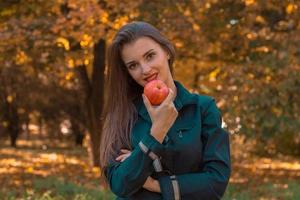 Schönes Mädchen mit langen Haaren steht im Park und hält Apfel in der Nähe des Mundes foto