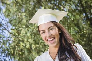 glückliches graduierendes Mischlingsmädchen in Mütze und Kleid foto