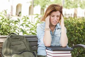 Studentin draußen mit Kopfschmerzen, die mit Büchern und Rucksack sitzt foto