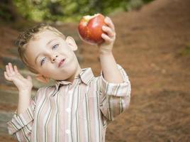 entzückender kleiner Junge, der draußen roten Apfel isst foto