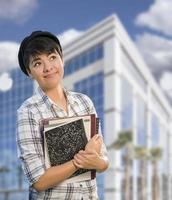 Studentin gemischter Abstammung, die Bücher vor dem Gebäude hält foto