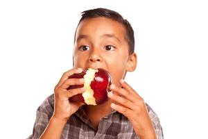 entzückender hispanischer Junge, der einen großen roten Apfel isst foto