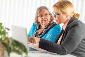 Frau, die älterer erwachsener Dame auf Laptop-Computer hilft foto