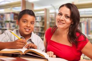 hispanischer kleiner Junge und famle Erwachsener, der in der Bibliothek studiert foto