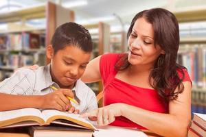 hispanischer kleiner Junge und famle Erwachsener, der in der Bibliothek studiert foto