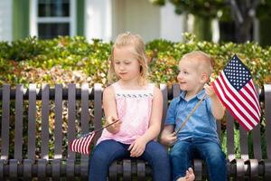 junge schwester und bruder vergleichen sich gegenseitig die größe der amerikanischen flagge auf der bank im park foto