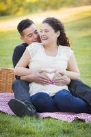 Schwangeres hispanisches Paar, das mit den Händen auf dem Bauch Herzform macht foto