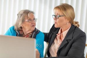 Frau, die älterer erwachsener Dame auf Laptop-Computer hilft foto