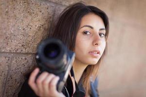 junger erwachsener ethnischer weiblicher fotograf gegen die wand, die kamera hält.