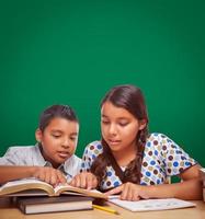 leere Kreidetafel hinter hispanischen Jungen und Mädchen, die Spaß beim gemeinsamen Lernen haben foto