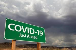 covid-19 coronavirus grünes verkehrsschild gegen ominösen stürmischen bewölkten himmel foto