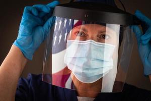 amerikanische flagge, die auf weibliches medizinisches personal mit schützender gesichtsmaske und schild reflektiert foto
