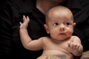 Junger Vater, der sein neugeborenes Baby der gemischten Rasse hält foto