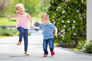 junge schwester und bruder halten sich an den händen und laufen im park foto