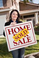 Frau mit verkauftem Immobilienschild vor Haus foto