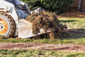 kleiner Bulldozer, der Gras vom Hof entfernt, um die Installation des Pools vorzubereiten foto