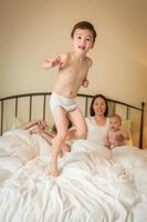 Chinesischer und kaukasischer Junge mit gemischten Rassen, der mit seiner Familie ins Bett springt foto