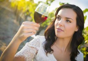 junge erwachsene frau, die ein glas wein im weinberg genießt foto