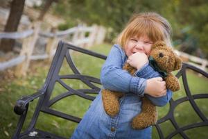 süßes lächelndes junges mädchen, das draußen ihren teddybär umarmt foto