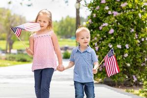 junge schwester und bruder schwenken amerikanische flaggen im park foto