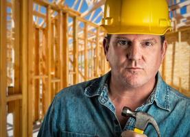 seriöser auftragnehmer mit helm, der hammer auf der baustelle hält. foto