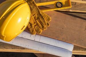 Zusammenfassung von Bauschutzhelmen, Handschuhen, Ebenen- und Hausplänen, die auf Holzplanken ruhen foto