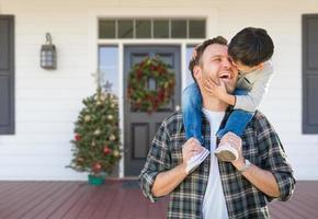 Junge reitet huckepack auf den Schultern des Vaters auf der weihnachtlich geschmückten Veranda foto