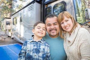 glückliche junge Mischlingsfamilie vor ihrem schönen Wohnmobil auf dem Campingplatz. foto