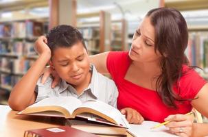 verärgerter hispanischer Junge und famle Erwachsener, der in der Bibliothek studiert foto