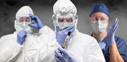 team von ärzten oder krankenschwestern in hazmat-ausrüstung, die ein positives coronavirus-reagenzglasbanner halten foto