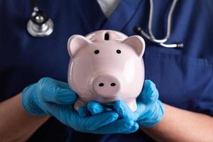 arzt oder krankenschwester, die chirurgische handschuhe tragen, die sparschwein halten foto