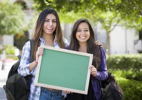 Studentinnen gemischter Abstammung, die eine leere Tafel halten foto