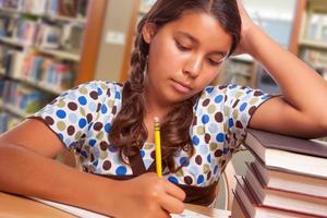hispanische Studentin mit Bleistift und Büchern, die in der Bibliothek studieren foto