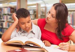 hispanischer kleiner Junge und famle Erwachsener, der in der Bibliothek studiert foto