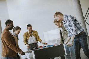 Junge lässige multiethnische Geschäftsleute, die Tischfußball spielen und sich im Büro entspannen foto