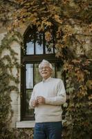 älterer Mann, der am Herbsttag am Fenster steht foto